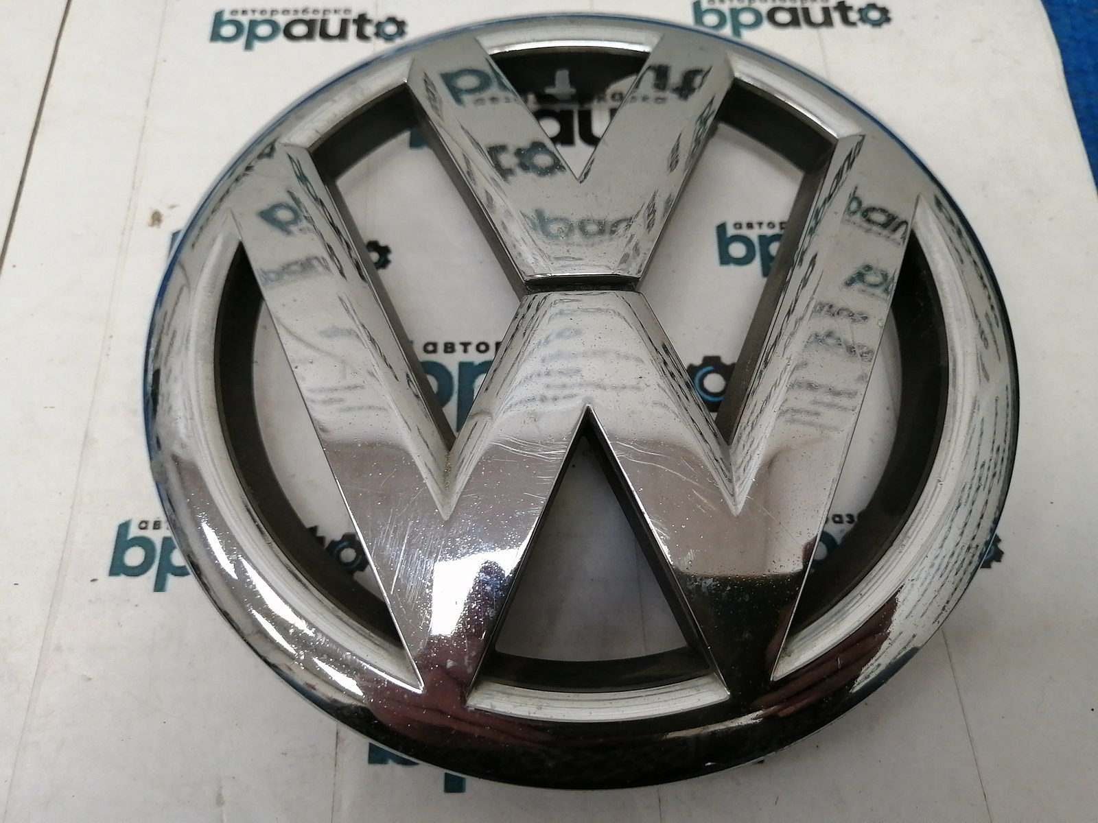 Фотография детали AA038051; Эмблема решетки радиатора (5K0853601) для Volkswagen Golf/БУ; Оригинал; Р1, Мелкий дефект; . Фото номер 1